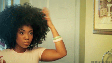 a GIF of a girl picking out her curly hair in the mirror