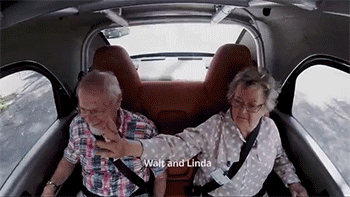 old couple riding in a self driving car is waving at the people they passed by