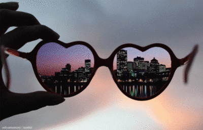 A cute girly GIF featuring a person holding up a pair of heart-shaped sunglasses