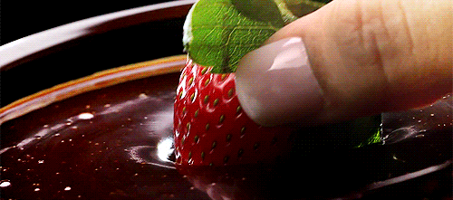 A woman dips a strawberry into chocolate sauce