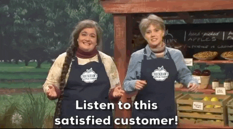 A gif of two ladies in front of a fruit stall saying "listen to this satisfied customer".