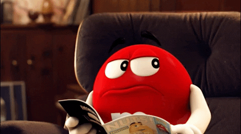 Gif of the red M&M reading a magazine. It then jumps off screen as it realises something.