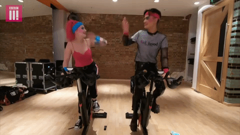 A GIF of a man and a woman cycling in a gym via Giphy