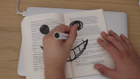 A hand drawing a smiley face and writing smile on an open book.