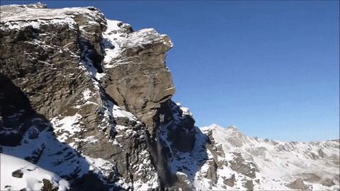 The cliffside collapses in dust and snow
