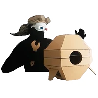Masked figure beside a handmade hexagonal cardboard drone