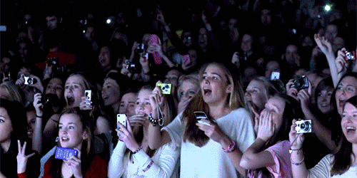 chica eufórica en un concierto mientras toma fotos con su celular