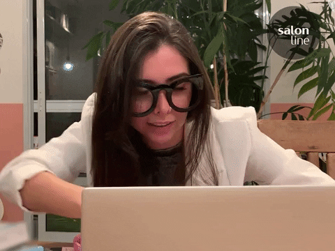 Mujer con lentes trabajando en la computadora saludando a la camara