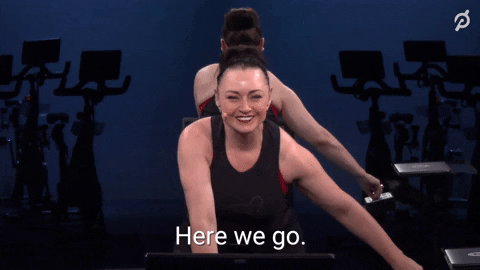 GIF of woman from Pelaton during spinning class saying "here we go"