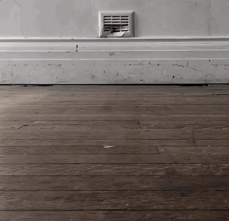 Slow moving GIF showing a wooden floor and white wall. Two bubbles float slowly up into the air. 