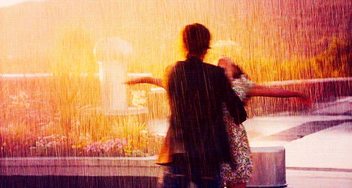 A man swings a lady with outstretched hands around in the rain. Via Giphy.com