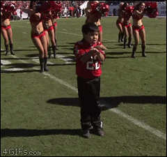 A young boy absolutely slaying a cheer routine, with a squad of professional cheerleaders also performing it just behind him