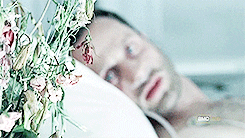 Rick reached for flowers while laying in a hospital bed.