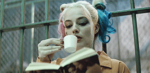 [Image description: Harley Quinn sipping from a small cup while reading a book] Via Giphy