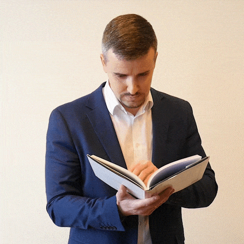 image animée de type GIF. Un homme en chemise blanche et veste bleu nuit feuillette avec intérêt le livre qu'il tient entre ses mains.