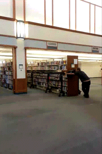 Library workers moving an entire bank of loaded bookshelves