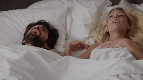 a blonde woman and bearded man in a white bed together