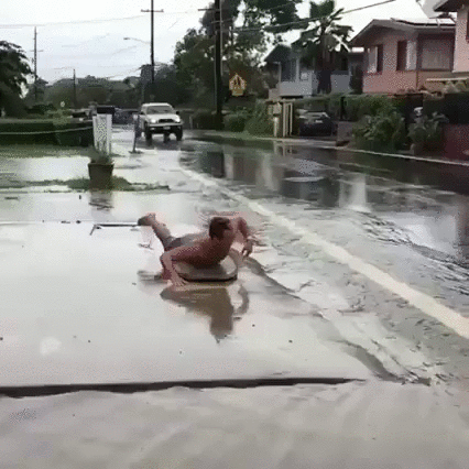 guy surfing "the pipe" on sidewalk as car splashes a wave