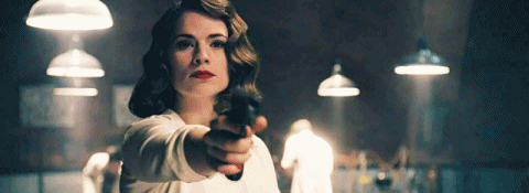 GIF of Peggy Carter (Hayley Atwell) shooting a handgun at Captain America/Steve Rogers (Chris Evans), who ducks behind his prototype shield