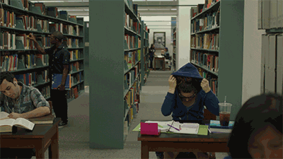 man pulls blue hood over his head and falls sideways on his table in the library