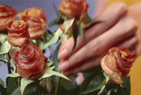 Animated gif of a bouquet of roses, but instead of petals, the flowers are rolled strips of bacon.