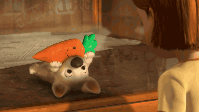 Image description: A gif of a scene from the movie. Bolt, as a pup, brings a toy that looks like a carrot to his human friend, Penny while wagging his tail.
