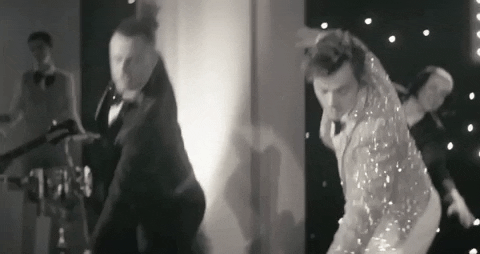 A black and white gif of Harry Styles in a tux performing a dance number with a similarly dress man.