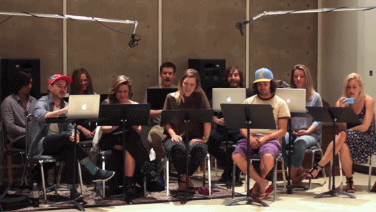 Choir group in a recording studio. Microphones are set up overhead and are visible. 