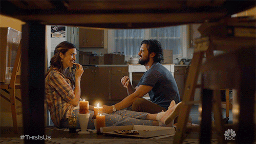  Couple sitting on the floor, eating pizza with candles lit around