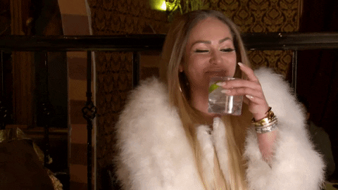 GIF of dressed up lady sipping on a cocktail while giggling