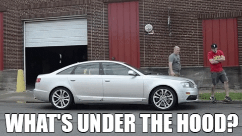 Two men walk up to a sedan and pop open the hood to look at the engine. A third joins them. The caption says, "What's under the hood?"