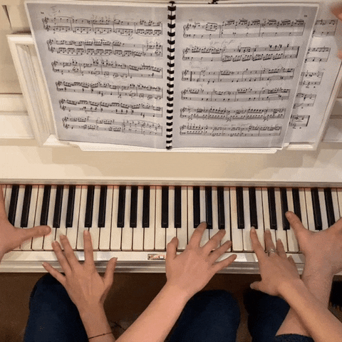 Five hands playing piano, one changing the sheet music page