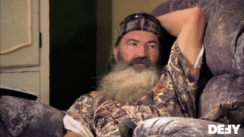 Bearded man in camouflage leaning back in an armchair, captioned 'None of this is real'