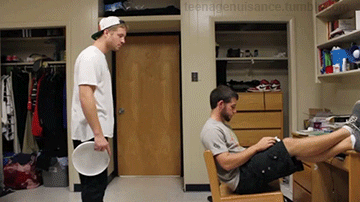 A college student is studying at his desk while his asshole roommate stands behind him and nonchalantly throws a frisbee at the back of the studying student's head saying, "hey, catch."