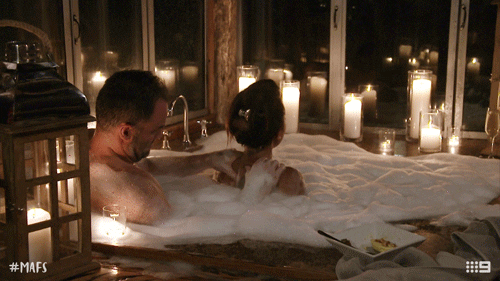 Man massaging a woman in a bathtub with candles lit around