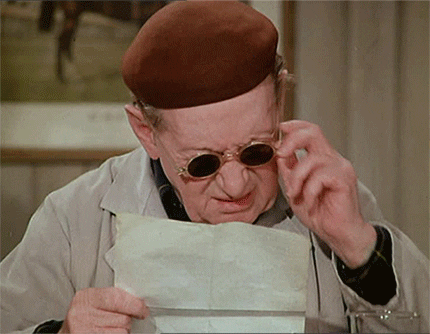 Elderly man taking off his sunglasses and squinting at a paper
