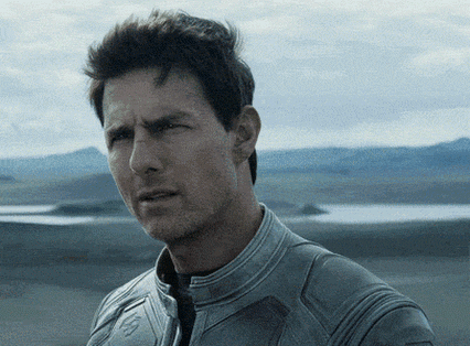 Tom Cruise standing in front of mountains looking confused. 
