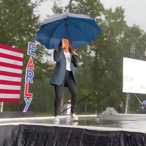 Kamala Harris dancing in the rain under a blue umbrella.