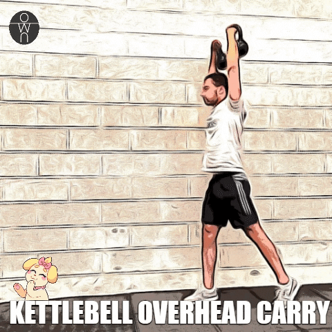 Un sportif tient deux kettlbell au-dessus de sa tête en marchant.