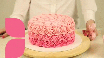 A woman is decorating a Quinceanera cake with pink frosting and sugar decorations.