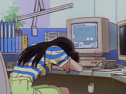 Uma garota de anime deitada em cima dos braços na frente de um computador, que está em cima de uma escrivaninha.