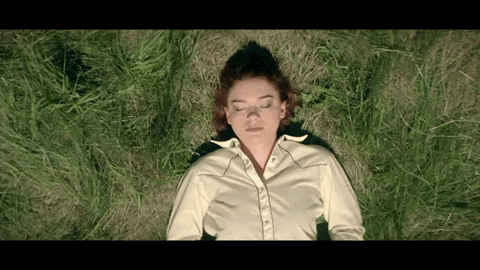 Woman lying on her back in long grass with her eyes closed