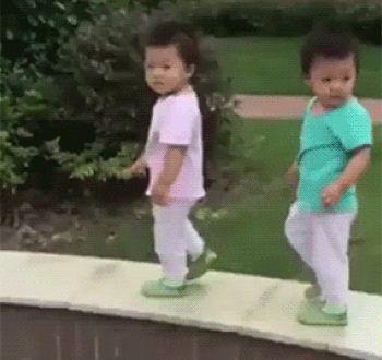 Duas crianças asiáticas estão andando devagarinho na beira de uma piscina e caem juntas.