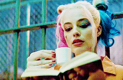 Movie character, Harley Quinn, sipping tea and reading while in jail