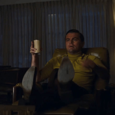 Once Upon a Time in Hollywood: Leonardo DiCaprio, drink in hand, sits up in his chair and points at the screen