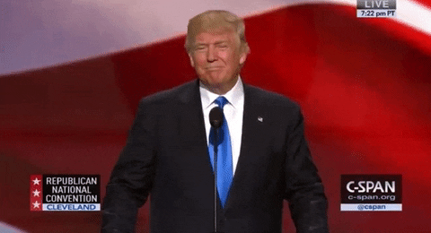 Donald Trump gives two thumbs up while speaking in front of a microphone. 