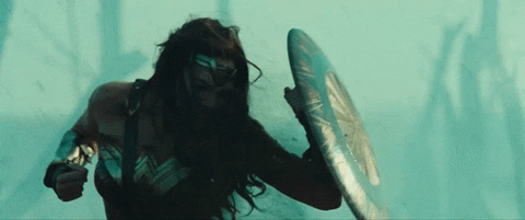 GIF of Wonder Woman (Gal Gadot) holding up her shield to protect herself from flying bullets on a battlefield.