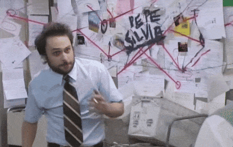 Charlie Day from It's Always Sunny in Philadelphia in front of a wall covered in papers and conspiracy strings, pointing frenetically