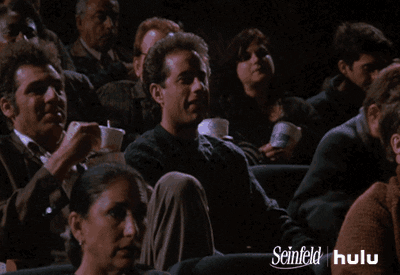 A man rubs his hands excitedly in a crowded theatre. 