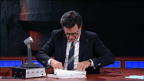 TV host Stephen Colbert rummaging through a pile of papers 